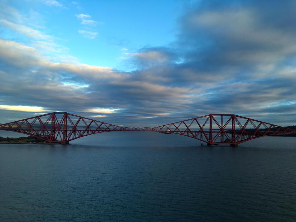 Looking straight on to the side of the rail bridge, with blue sky and grey clouds behind it.